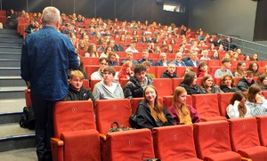Mężczyzna mówiący do młodzieży siedzącej w sali kinowej.