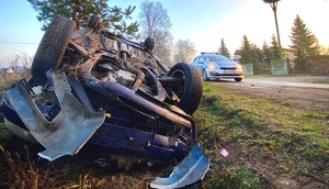 Samochód leżący na dachu i radiowóz obok na drodze.
