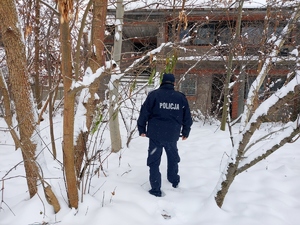 Policjant idący w kierunku pustostanu w tle aura zimowa.