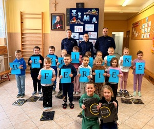 Policjanci i dzieci z napisem bezpieczna szkoła oraz elementami odblaskowymi.