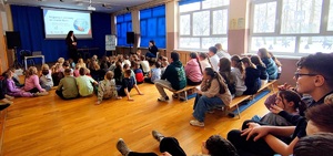 Pracownik sanepidu przed dziećmi w tle prezentacja o zdrowym trybie życia.