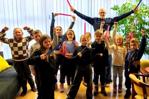 Komendant wraz z dziećmi wszyscy trzymają w gorę ręce z odblaskami.