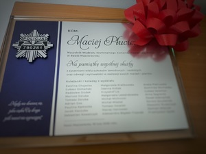 Tabliczka pamiątkowa z podziękowaniami dla komisarza Macieja Płuciennika z podziękowaniami za wspólną służbę, gwiazda policyjna z cyframi 790281 oraz kokarda.