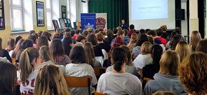 Policjantka z mikrofonem mówi do młodzieży siedzącej na krzesłach.