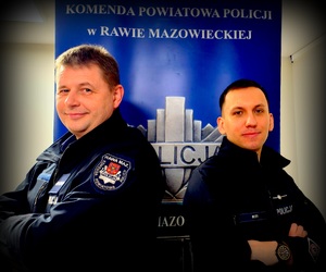 Dwóch policjantów stojących plecami do siebie w tle napis Komenda Powiatowa Policji w Rawie Mazowieckiej.
