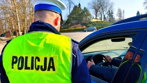 Policjant obok samochodu widać ręce na kierownicy.