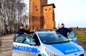 Policjanci przy radiowozie na tle zamku.