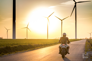 Motocyklista na tle wiatraków i zachodzącego słońca.