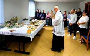 Ksiądz przy stole z pokarmami policjanci i pracownicy obok.
