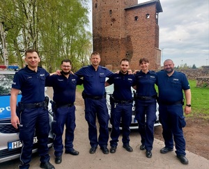 Policjanci stojący obok siebie na tle ruin zamku i radiowóz obok.