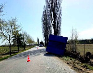 Przewrócony kontener z korzeniami, pachołek na drodze i w tle radiowóz.