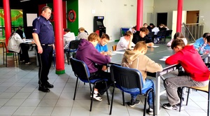 Policjant stojący obok dzieci piszących test wiedzy.