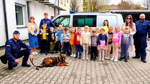 Dzieci, policjanci, nauczyciele i policjant z psem na tle radiowozu