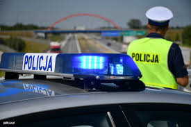 Policjant ruchu drogowego obok radiowozu patrzy na jezdnię .