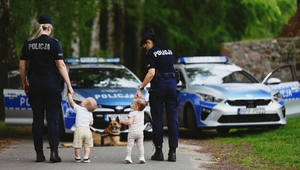 Policjantki z dziećmi na tle radiowozów.