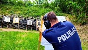 Policjant z bronią celujący do tarczy na strzelnicy z za zasłony.