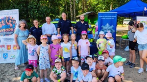 Policjanci i burmistrz oraz nauczycielka stoją razem z dziećmi przy radiowozie.
