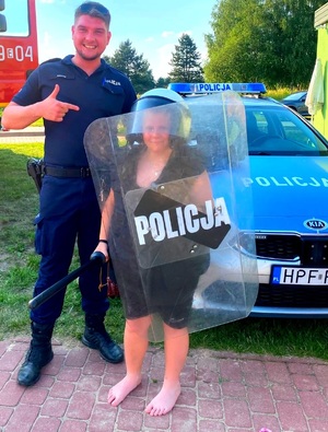 Policjant, radiowóz i dziecko w  tarcza policyjna w kasku.