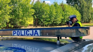 Policjant patrzący w miernik prędkości i dach radiowozu.