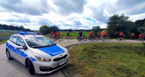 Radiowóz na drodze i uczestnicy rajdu na rowerach.