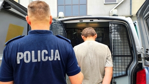 Policjant z zatrzymanym przy radiowozie.