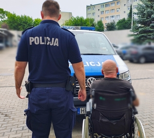 Policjant  zatrzymanym na wózku inwalidzkim na tle radiowozu.