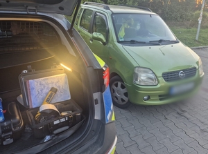 Samochód oraz radiowóz z otwartym bagażnikiem, w którym jest urządzenie do badania trzeźwości.