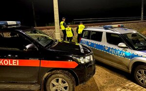 Funkcjonariusze Straży Ochrony Kolei oraz policjantka stoją przy torach obok dwa radiowozy.